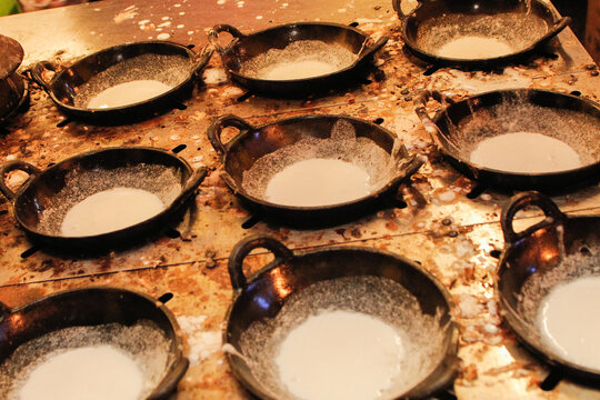 Traditional Indonesian serabi batter cooking in small clay pans, capturing an authentic street food process with rustic texture.