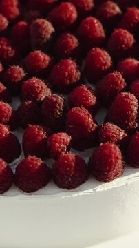 Vertical video. Detailed view of a raspberry-covered wedding cake with white cream frosting outdoors.