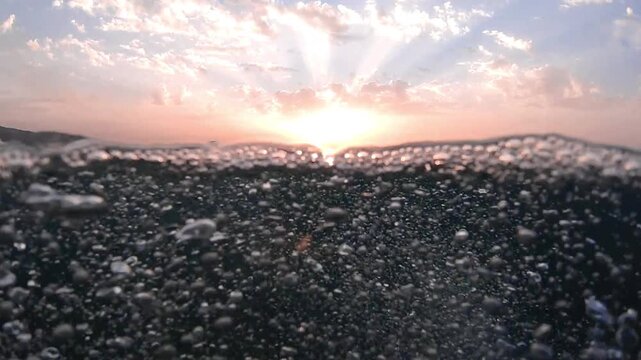 Underwater part and sunset skylight splitted by waterline, underwater bubbles. Beautiful clouds and bright sun over sea water, Real image very suitable for backgrounds in Mediterranean sea, undersea.