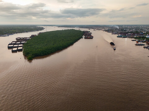 Aerial view of Pulau Kembang island surrounded by the Barito River with coal barges and tugboats navigating the waterway in Alalak, South Kalimantan, Indonesia.