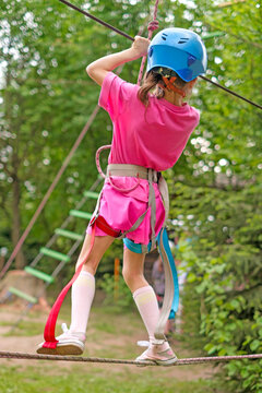 A girl goes through a suspended obstacle course, holding on to a rope. Rope Park of Amusement and Outdoor Activities