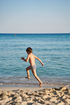 A cheerful child sprints along the water's edge of a beautiful tropical sea, enjoying carefree outdoor play on a sunny morning.
