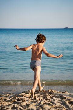 A cheerful child sprints along the water's edge of a beautiful tropical sea, enjoying carefree outdoor play on a sunny morning.