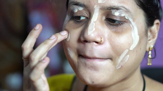 Indian Woman Applying Liquid Foundation Cream on Face with Fingers. South Asian Woman Doing Daily Cosmetic Beauty and Makeup Routine. Facial Skin Care Tutorial with Liquid Base Makeup.