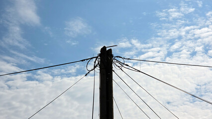 Fototapeta premium Silhouette of wooden utility pole with tangled telecommunication cables against cloudy sky