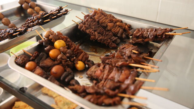 Traditional Indonesian skewered offal and braised eggs displayed on a food stall tray, authentic street food photography with rich savory appeal.