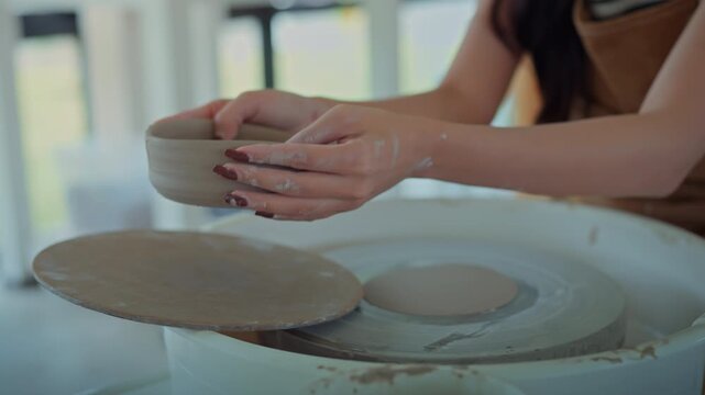 Close up of Asian woman hands shaping clay bowl on pottery wheel at studio workshop, creative female artisan making ceramic product for hobby, small business entrepreneur, traditional handicraft