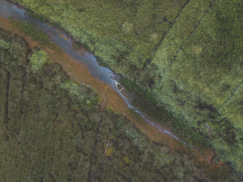 Aerial view of a small traditional boat moored in a narrow channel within the lush green marshlands of the Aveiro Lagoon in Aveiro District, Portugal.