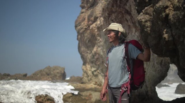 Backpacker walking across rocky shoreline cliffs, exploring a scenic tropical coast during a solo travel adventure by the beach