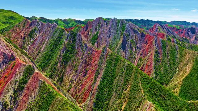 Colorful Danxia landform mountains with vibrant red and green slopes under blue sky in Xinjiang, China.