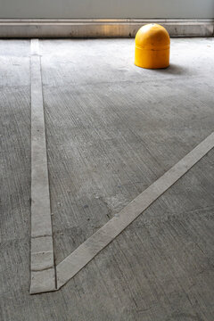 Bright yellow safety bollard and white painted lines on an empty concrete parking garage floor.