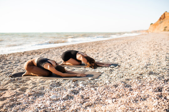Two teenage girls 15-16 year old doing yoga class lying at beach over sea background in sunny day. Healthy active lifestyle. Teenagerhood. Summer season. Relaxation.