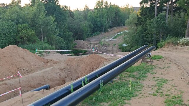 Large black gas pipes placed beside a deep trench on a construction site during pipeline installation works