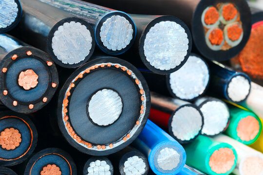 Close-up view of multiple electrical cables. Black cables show copper cores and white insulation. Blue and green cables have distinct internal designs. Colorful insulation aids in cable identification