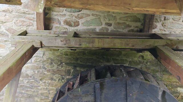 Old wooden water wheel preserved under a small roof beside a stone wall at a traditional mill