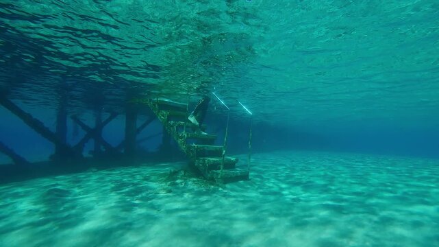Woman snorkeler in wetsuit goes down the stairs from pier, puts on fins and swims on surface of turquoise water, Slow motion, Underwater shot