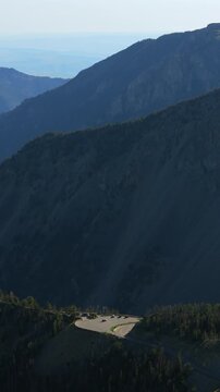 Vertical Screen: Beartooth Highway in Montana USA featuring dramatic mountain slopes with forested ridges and scenic overlook parking area surrounded by evergreen trees and rugged terrain.