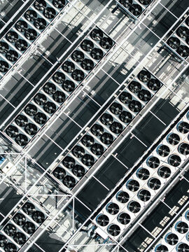 Aerial view of a large array of industrial cooling fans and HVAC units arranged in rows on a flat rooftop in Riga, Latvia.