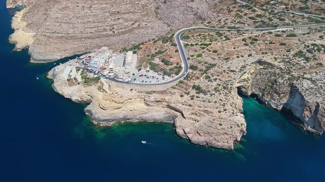 At Malta's Blue Grotto near Qrendi and Żurrieq, a sea arch and surrounding limestone cliffs rise over clear turquoise water along the rocky coastline, viewed from a drone.