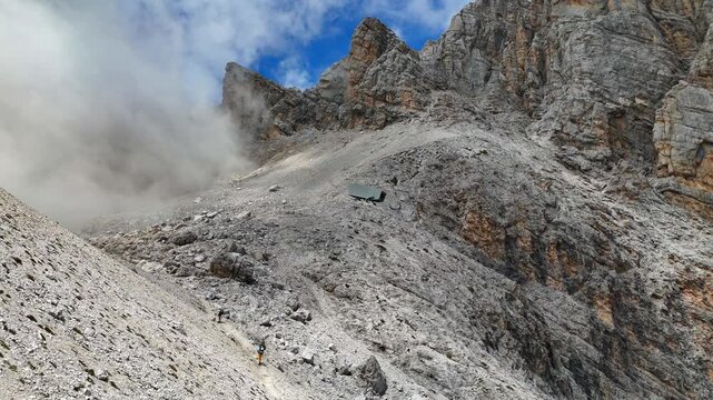 Hikers  walking along a steep rocky mountain trail surrounded by dramatic cliffs and clounds.  Majestic Dolomite Mountains. 