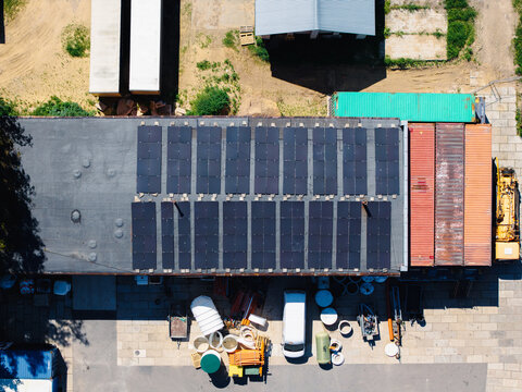 Aerial view of solar panels installed on a flat industrial roof with shipping containers and a white van parked below in Ulbroka, Ropazi Municipality, Latvia.