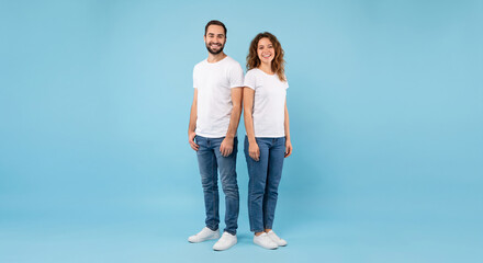 Fototapeta premium Happy Young Couple in White T-shirts Standing Against Blue Background in Studio