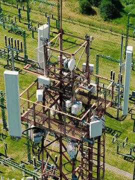 Aerial view of a telecommunications tower equipped with multiple antennas and electronic equipment, located within an electrical substation area in Garkalne, Adazi Municipality, Latvia.