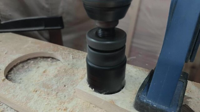 Anonymous self employed entrepreneur in workwear finishing drilling circular wooden discs from clamped plywood with heavy power tool on studio workbench during extreme close up pulling back shot