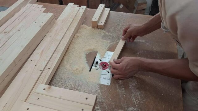 Authentic High Angle View Of Unrecognizable Carpenter In Full PPE Gear Leaning Over Router Table To Inspect And Mill Wooden Block On Dusty Workbench Inside Local Joinery Studio Documentary B-Roll