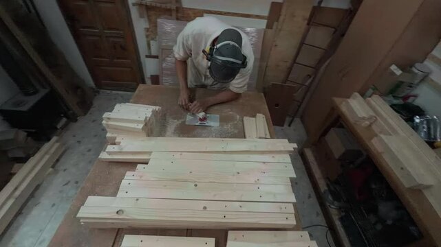 Authentic High Angle Wide Shot Of Unrecognizable Carpenter Wearing Full PPE Safety Gear Milling Edge Of Small Wooden Block On Built In Router Table Inside Rustic Joinery Studio Handheld B-Roll