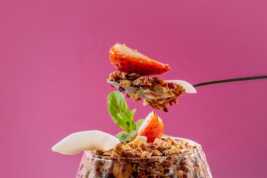 Healthy Granola Yogurt Parfait with Fresh Strawberry, Mint and Coconut Flakes on Pink Background