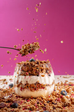 Granola Yogurt Parfait with Blueberries and Falling Crunchy Muesli on Pink Background