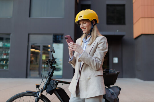 Young businesswoman checks her phone while standing next to her electric bicycle in the city