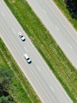 Aerial view of the A2 highway with two cars traveling along the asphalt road surrounded by green grass and trees in Riga, Adazi Municipality, Latvia.