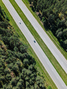 Aerial view of the A2 highway cutting through a dense pine forest with cars driving on the asphalt road in Riga, Adazi Municipality, Latvia.