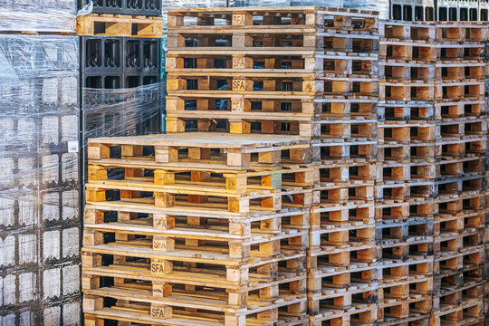 Valmiermuiza, Latvia - July 03, 2026: Stacked wooden pallets in a warehouse with plastic wrap and a wall of black crates visible in the background