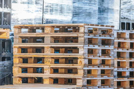 Valmiermuiza, Latvia - July 03, 2026: Stacked wooden pallets with visible branding in a warehouse setting, surrounded by plastic-wrapped goods and industrial materials