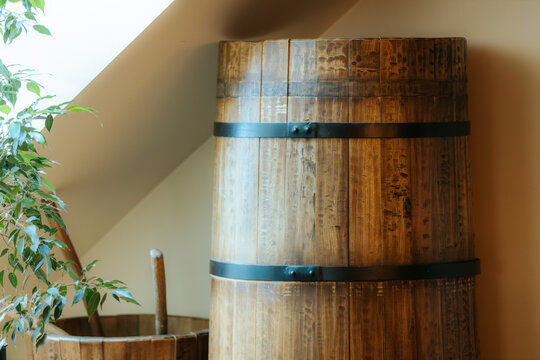 Wooden barrels with metal bands positioned near a window, accompanied by a smaller barrel and a potted plant in a cozy indoor setting