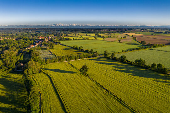 Aerial view of the rural landscape of Zelata featuring lush green fields, scattered trees, and a small village against a backdrop of distant mountains in Zelata, Lombardy, Italy.
