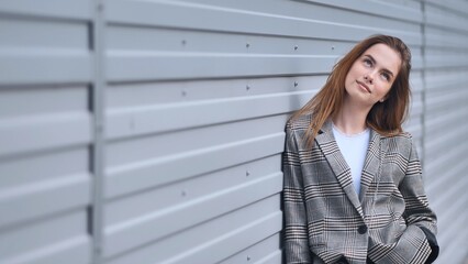 Fototapeta premium Stylish businesswoman in checkered jacket looking up, contemplating new opportunities, leaning against a modern metal wall