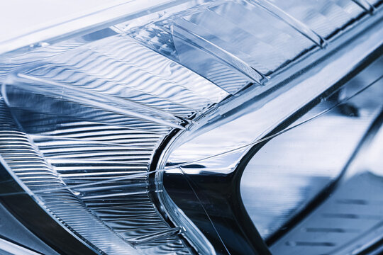 Modern car headlight fills the frame in close view. Automotive technology background features reflective surfaces and detailed lamp design. Clean vehicle lighting creates a sleek industrial texture.