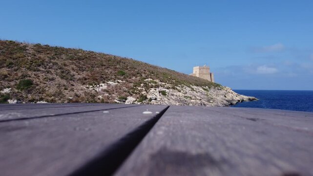 Aerial view of the historic Xlendi Tower standing on a rocky peninsula overlooking the blue Mediterranean Sea and coastal cliffs in Munxar, Gozo Region, Malta. High quality 4k footage