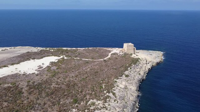 Aerial view of the historic Xlendi Tower standing on a rocky peninsula overlooking the blue Mediterranean Sea and coastal cliffs in Munxar, Gozo Region, Malta. High quality 4k footage