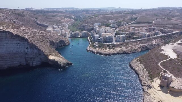Aerial view of Xlendi Bay featuring the historic watchtower on the rocky cliffs and coastal buildings in Munxar, Gozo Region, Malta. High quality 4k footage