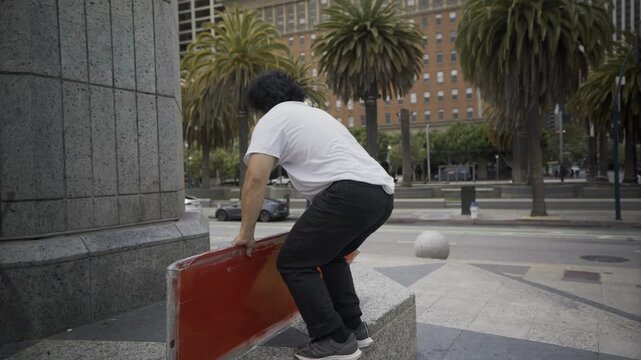 Man Holding Red Board On Granite Column Base In San Francisco Plaza - Slow Motion