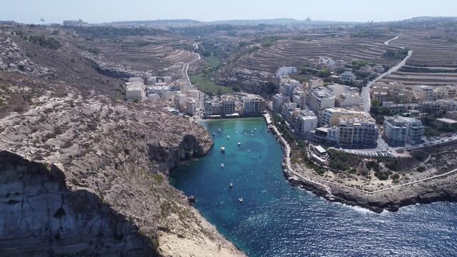 Aerial view of Xlendi Bay featuring the historic watchtower on the rocky cliffs and coastal buildings in Munxar, Gozo Region, Malta. High quality 4k footage