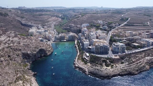 Aerial view of Xlendi Bay featuring the historic watchtower on the rocky cliffs and coastal buildings in Munxar, Gozo Region, Malta. High quality 4k footage