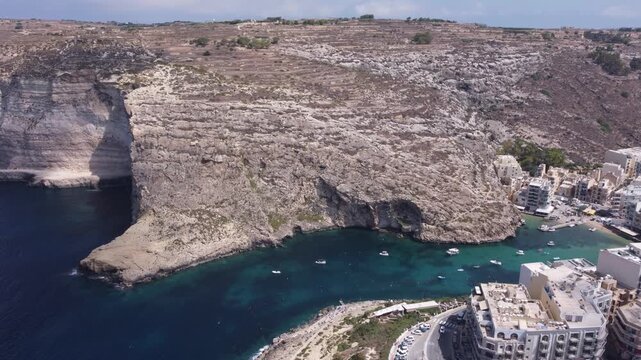 Aerial view of Xlendi Bay featuring the historic watchtower on the rocky cliffs and coastal buildings in Munxar, Gozo Region, Malta. High quality 4k footage