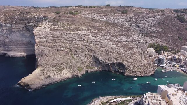 Aerial view of Xlendi Bay featuring the historic watchtower on the rocky cliffs and coastal buildings in Munxar, Gozo Region, Malta. High quality 4k footage