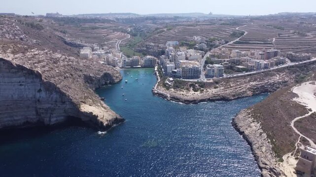 Aerial view of Xlendi Bay featuring the historic watchtower on the rocky cliffs and coastal buildings in Munxar, Gozo Region, Malta. High quality 4k footage